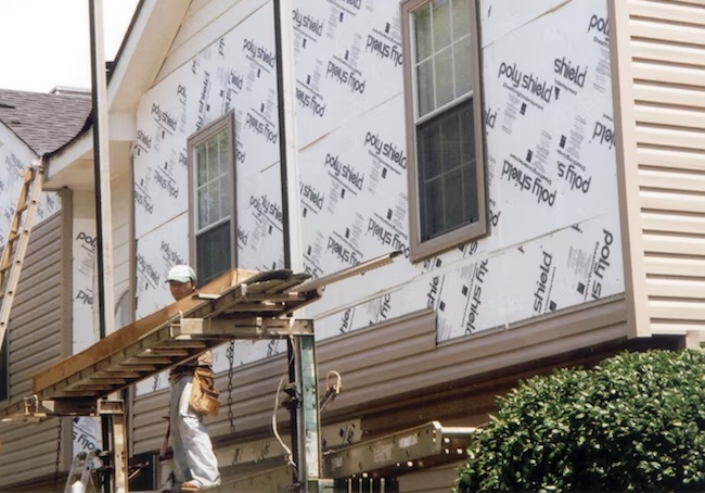 White rigid foam board insulation on home siding with construction workers.